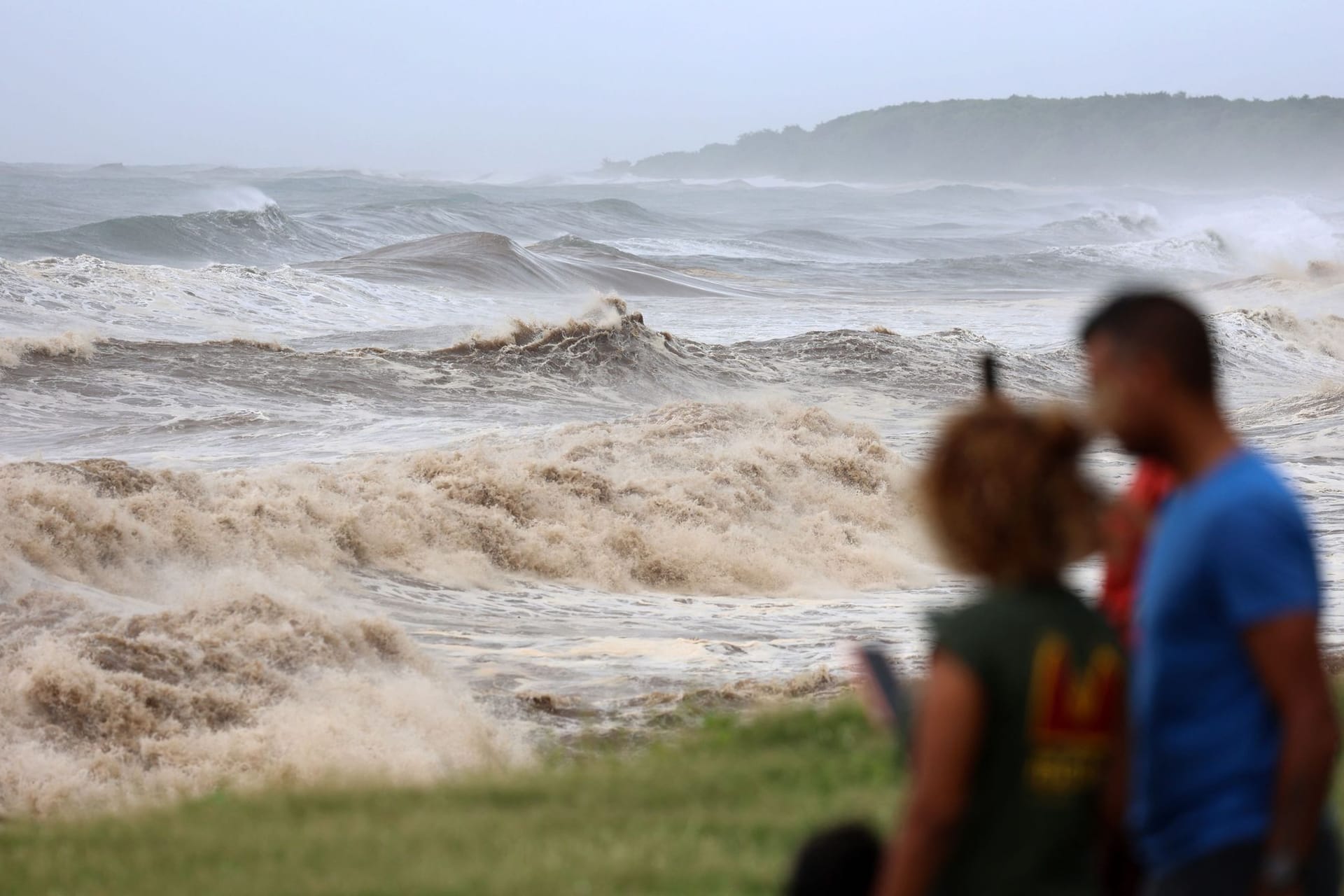 La Réunion: Zwei Personen fotografieren die hohen Wellen von der Strandpromenade aus.