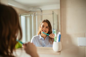 Frau putzt Zähne vor einem Spiegel