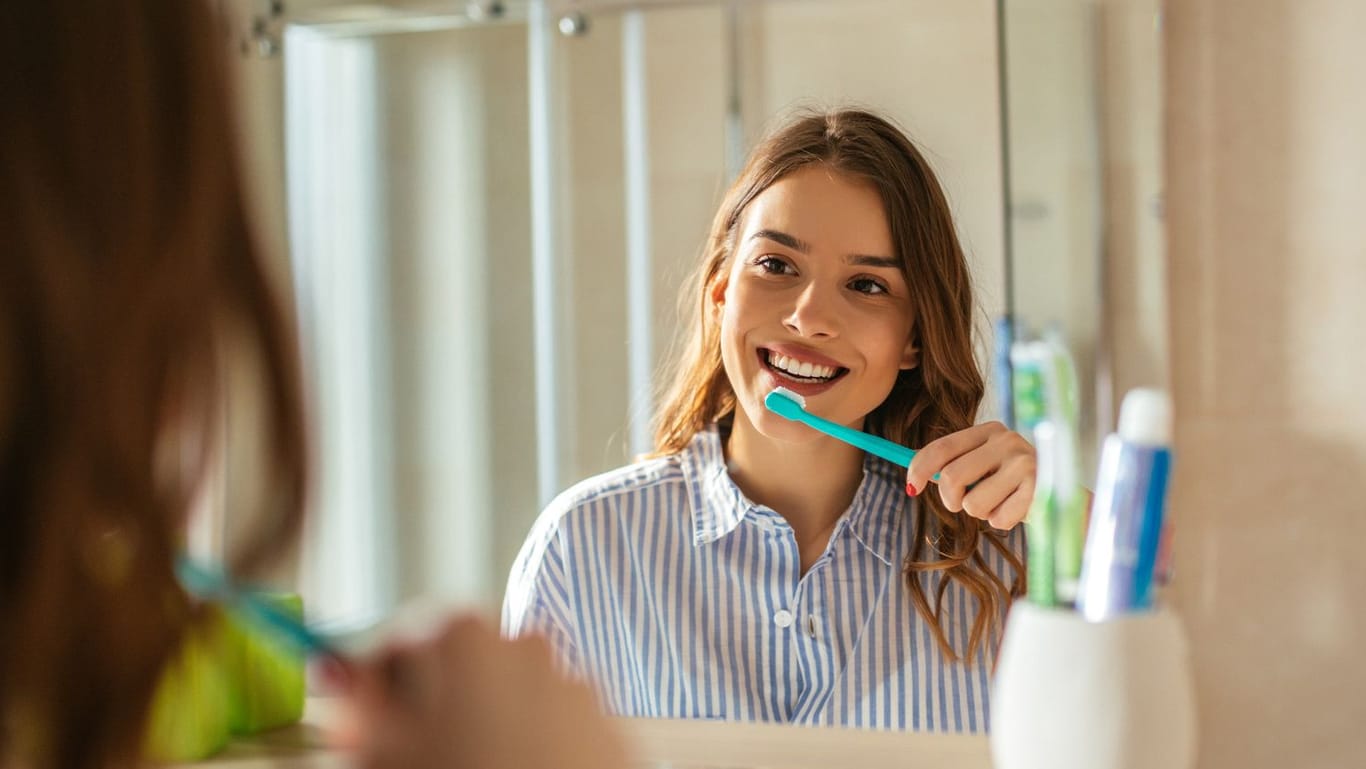 Frau putzt Zähne vor einem Spiegel