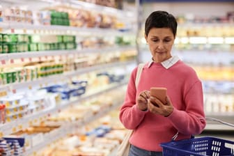 Frau im Supermarkt schaut auf ihr Handy