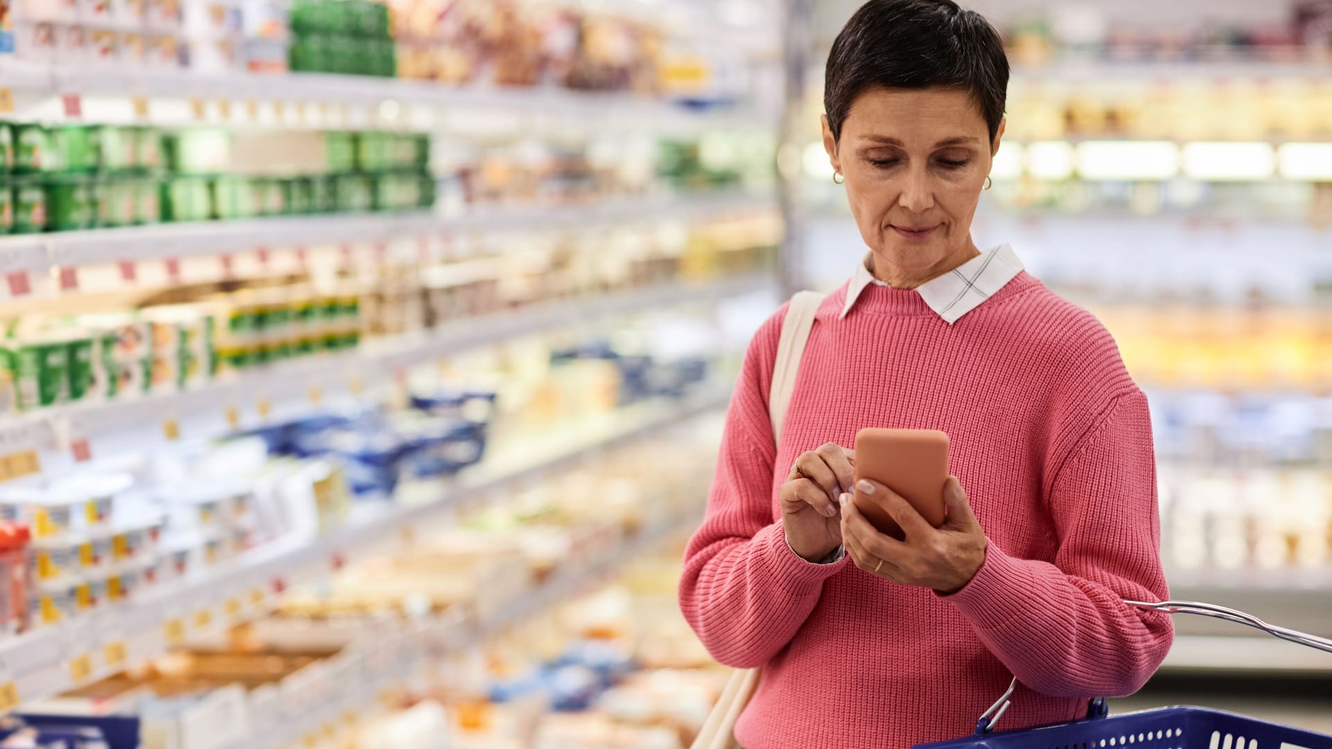 Frau im Supermarkt schaut auf ihr Handy