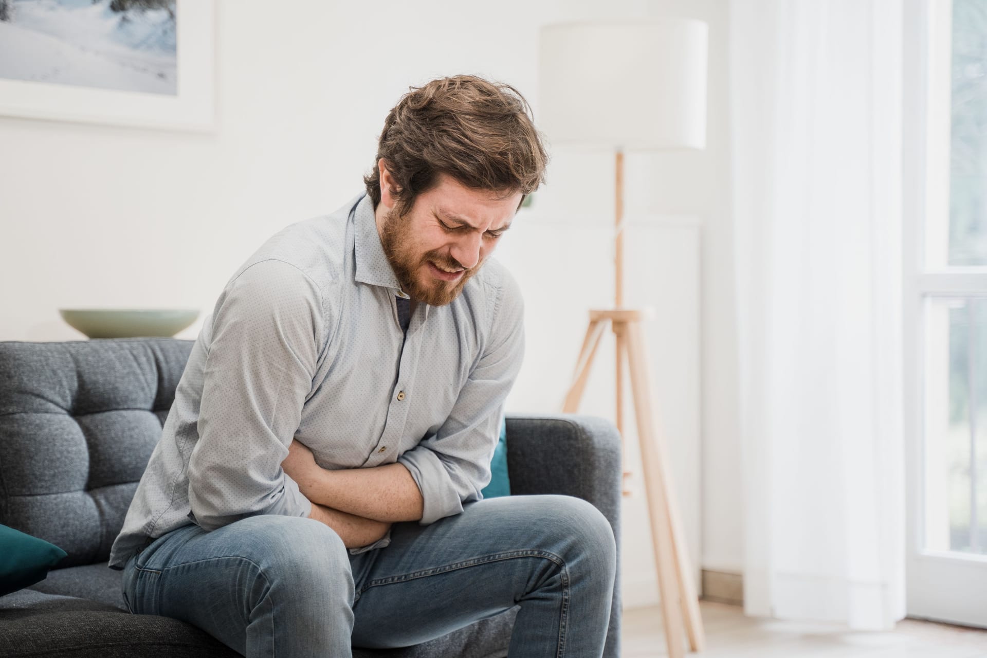 Mann sitzt mit Bauchweh auf dem Sofa