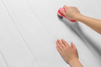 Woman cleaning white mattress with brush, closeup. Space for text
