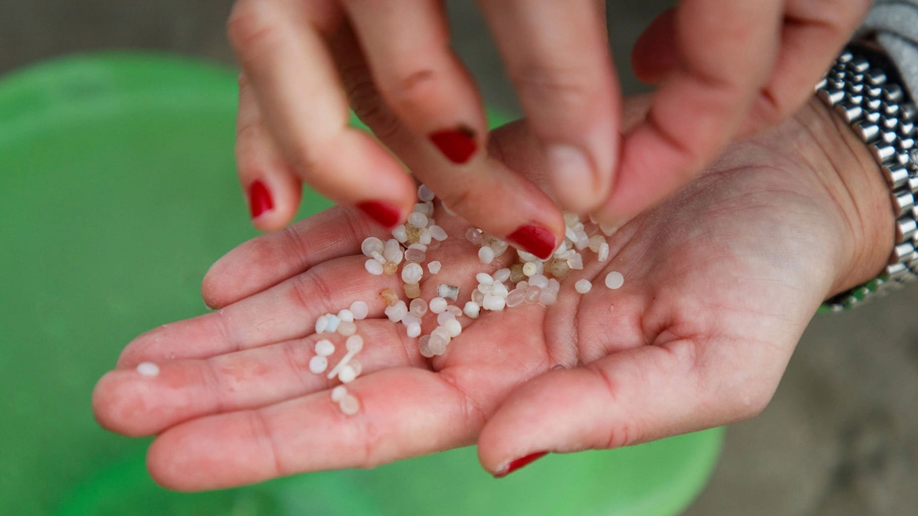 Spanien, Nigran: Ein freiwilliger Helfer hält Plastikkügelchen in der Hand, die an einem Strand gesammelt wurden.