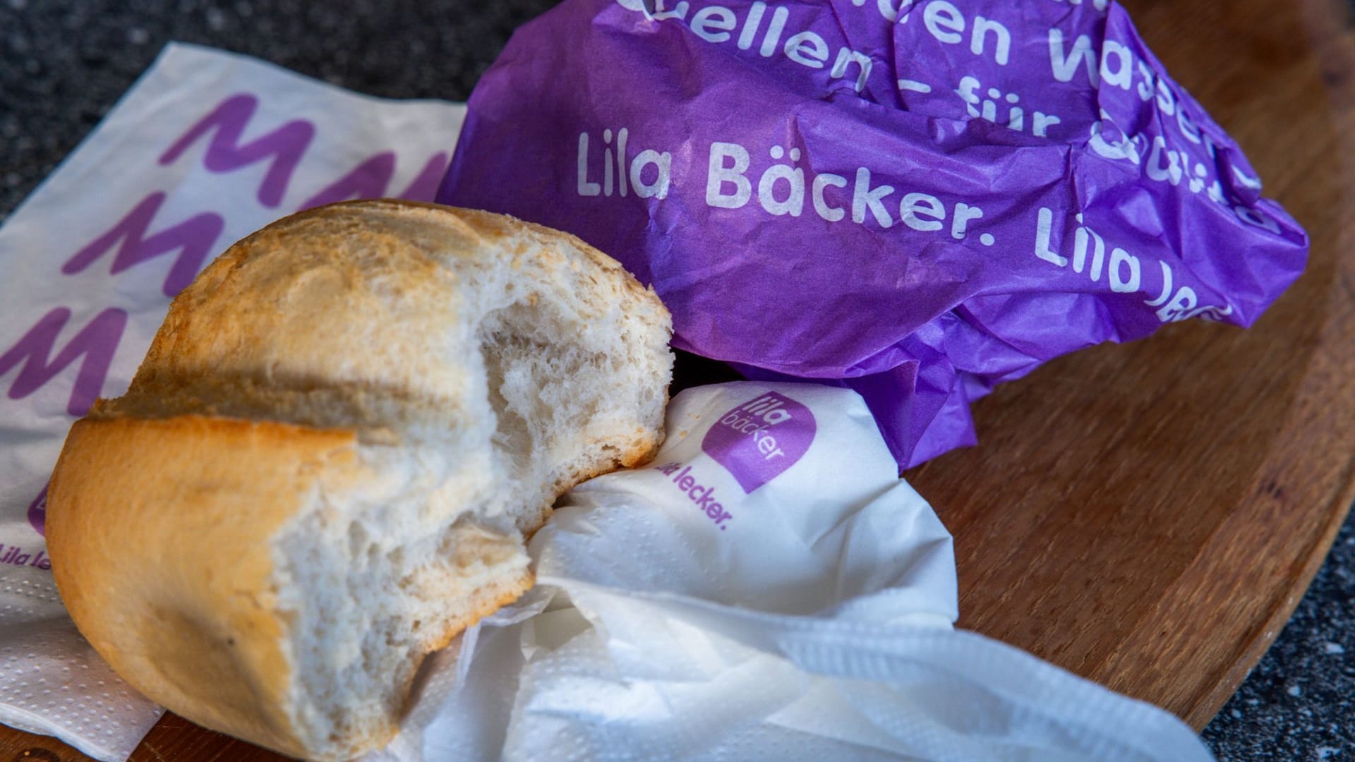 Eine zerknüllte Brottüte von Lila Bäcker neben einem Brötchen (Symbolbild): Dem Unternehmen sei es nicht gelungen, die Logistik in seinem großen Einzugsgebiet gut zu organisieren.