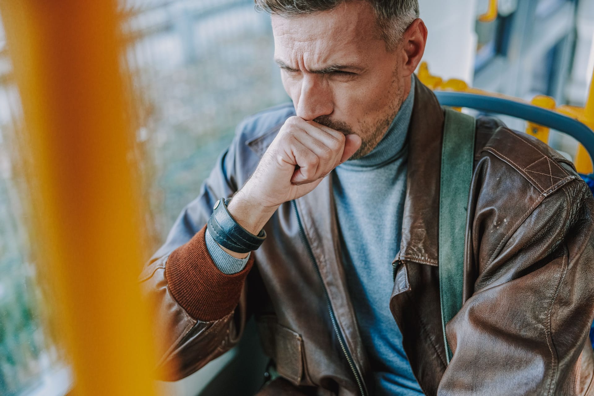 Ein Mann sitzt in der Straßenbahn und hustet