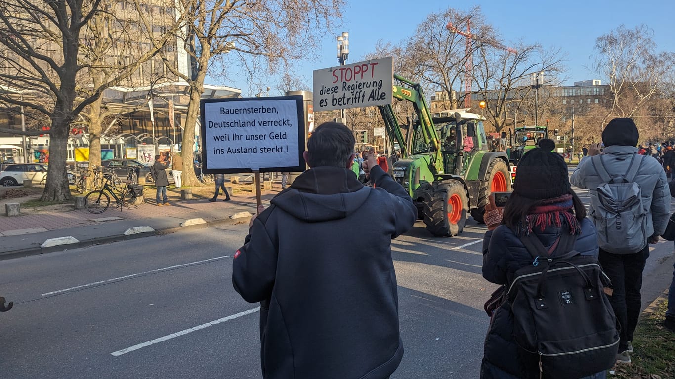 Bauernprotest in Frankfurt am Main: Ein Demonstrierender hält ein Schild hoch, während ein Traktor an ihm vorbeifährt.