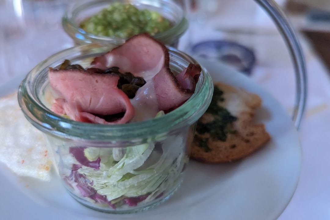 Vorspeise für die Gäste am Tisch: Rosa gegarter Tafelspitz, serviert mit Crackern und einer Garnelen-Sülze auf einem Bett aus Kokos-Garnelengras-Mousse.