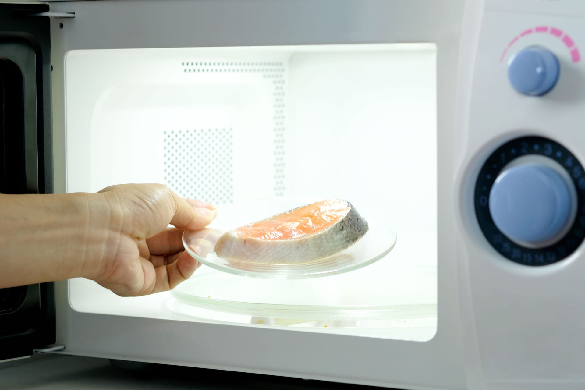 Hand of housewife are cooking steak fish with microwave oven for dinner with her family. She prepared by putting fish dish into microwave oven and then she serve health food. Cooking food concept.