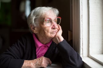 Rentnerin sitzt allein zu Hause und schaut aus dem Fenster