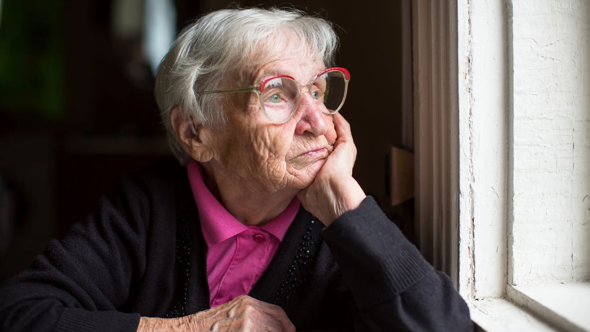 Rentnerin sitzt allein zu Hause und schaut aus dem Fenster