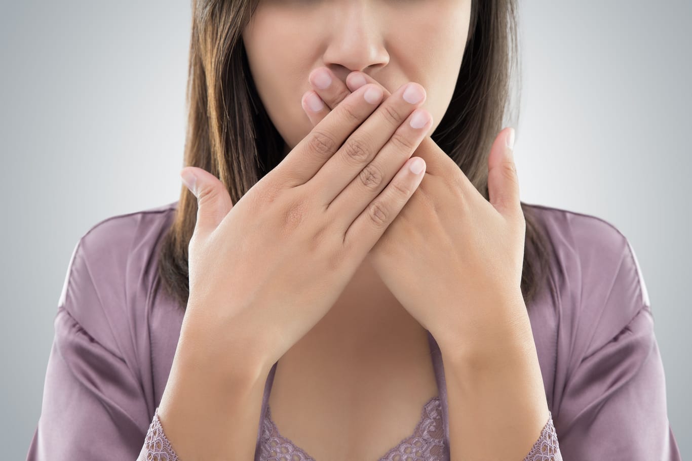 Eine Frau bedeckt den Mund mit den Händen: Stellt sich Schluckauf ständig ein, ist das Betroffenen oftmals unangenehm.