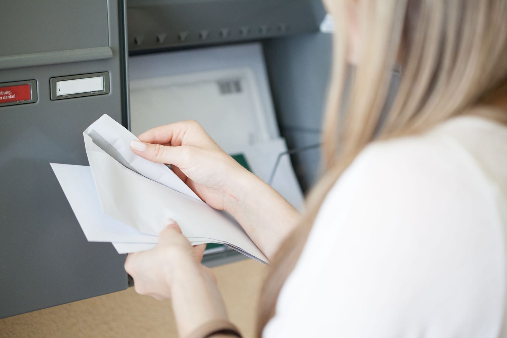 Person holt Post aus Briefkasten und liest Schreiben