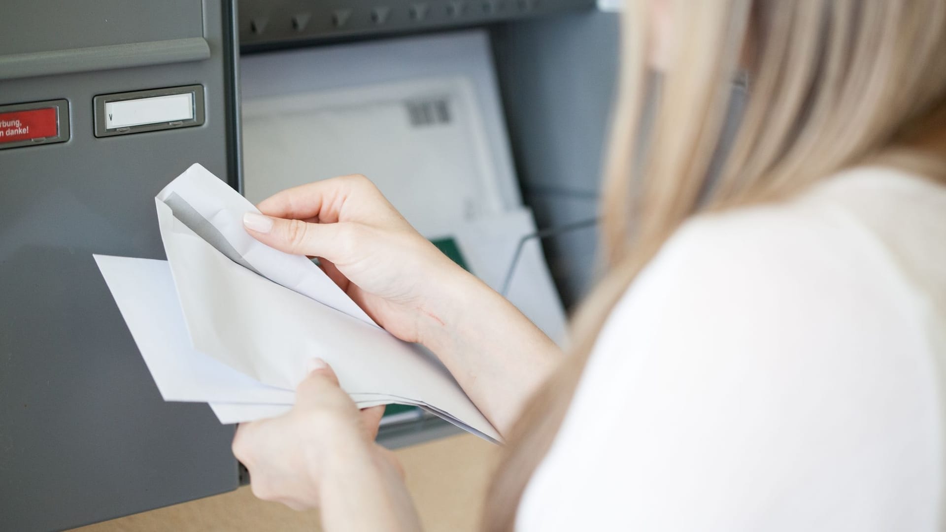 Person holt Post aus Briefkasten und liest Schreiben