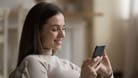 Young smiling woman spend leisure at home using modern smartphone