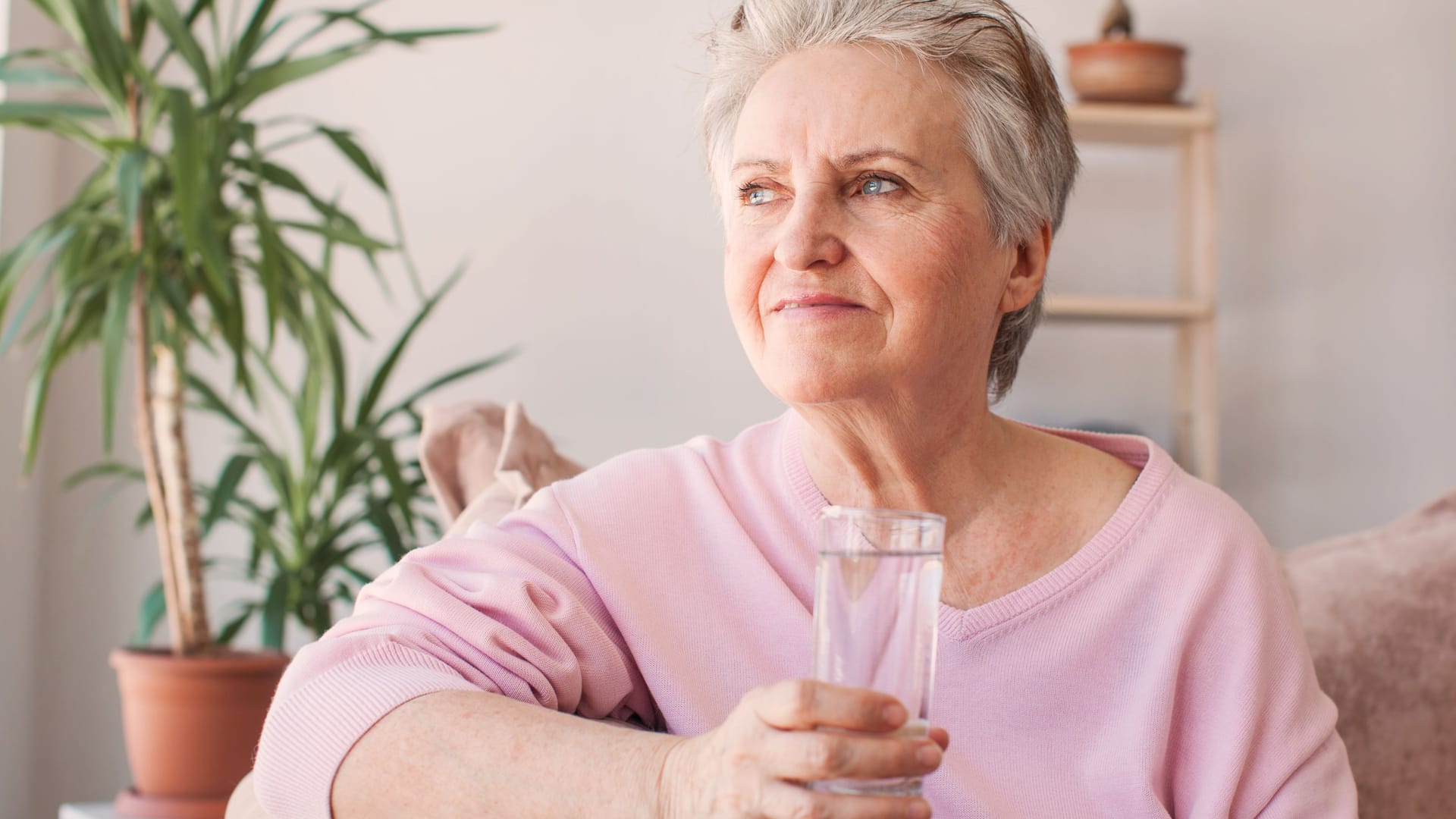 Eine Frau sitzt auf dem Sofa und trinkt ein Glas Wasser.