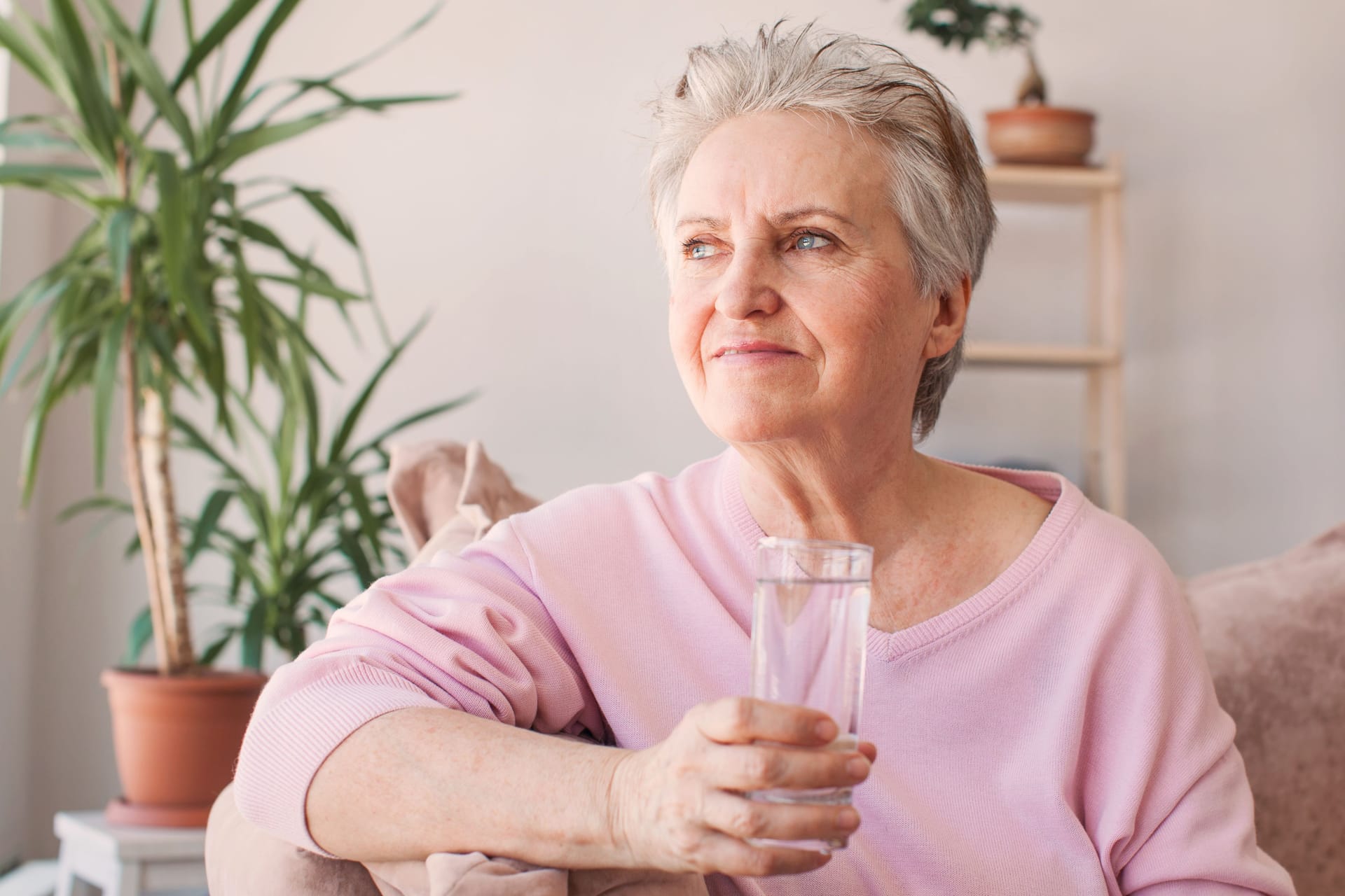 Eine Frau sitzt auf dem Sofa und trinkt ein Glas Wasser.