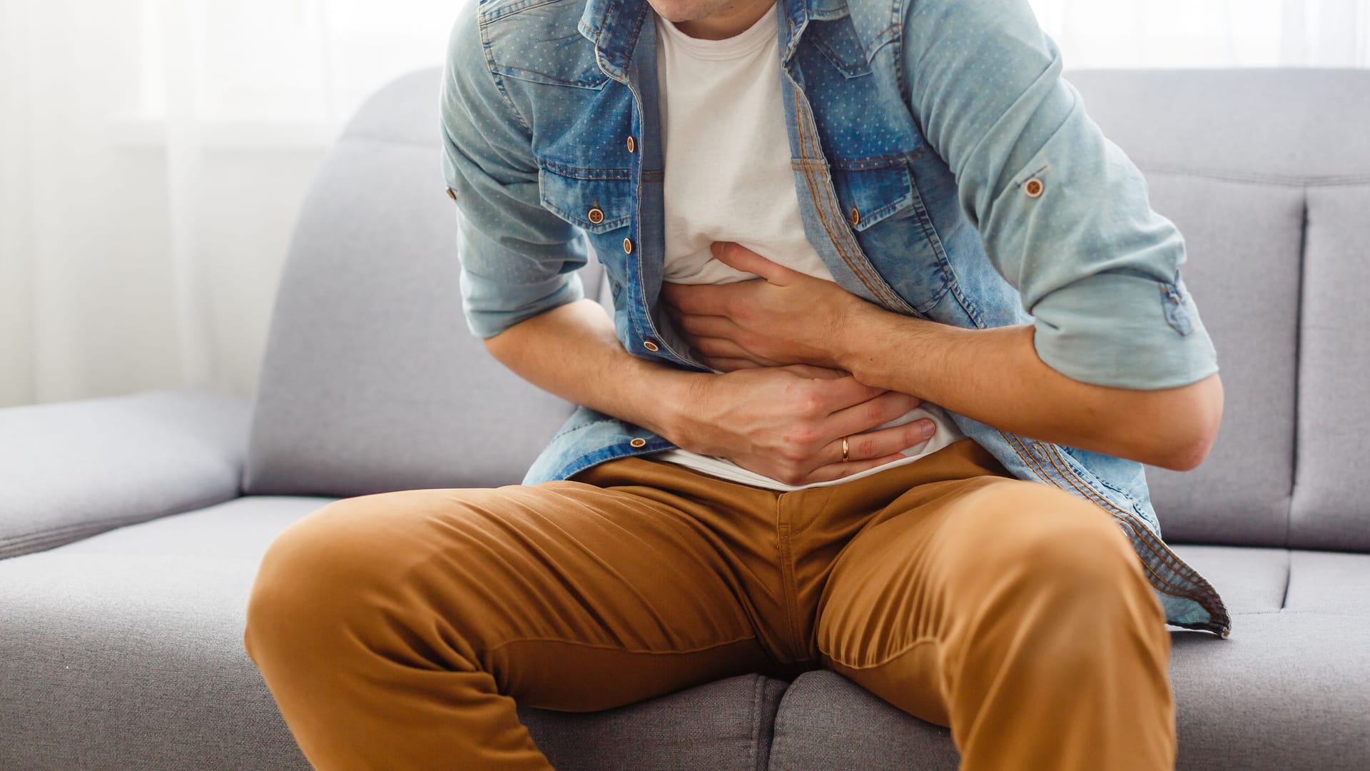 Junger Mann sitzt auf dem Sofa und hält sich den Bauch