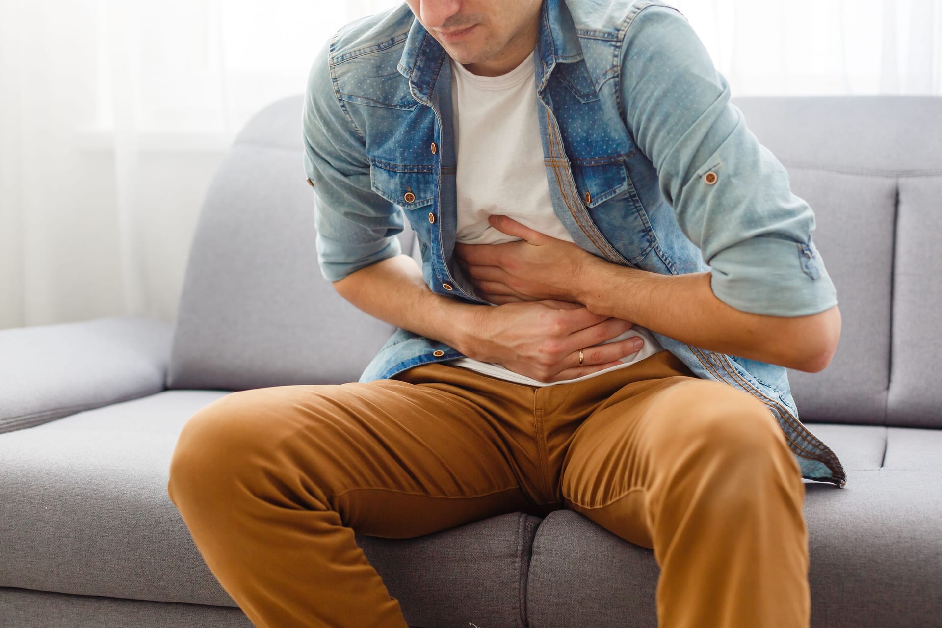 Junger Mann sitzt auf dem Sofa und hält sich den Bauch