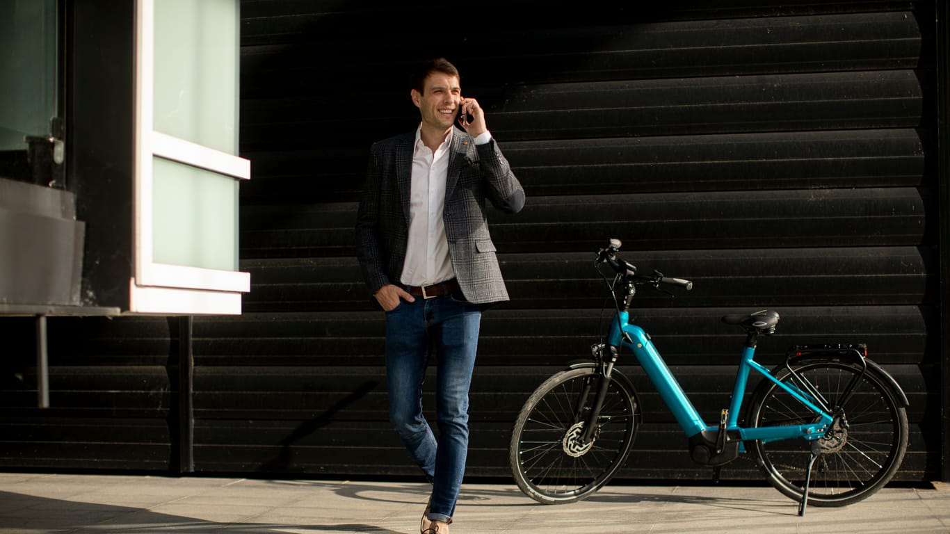 Young businessman walking away from the ebike and using mobile phone