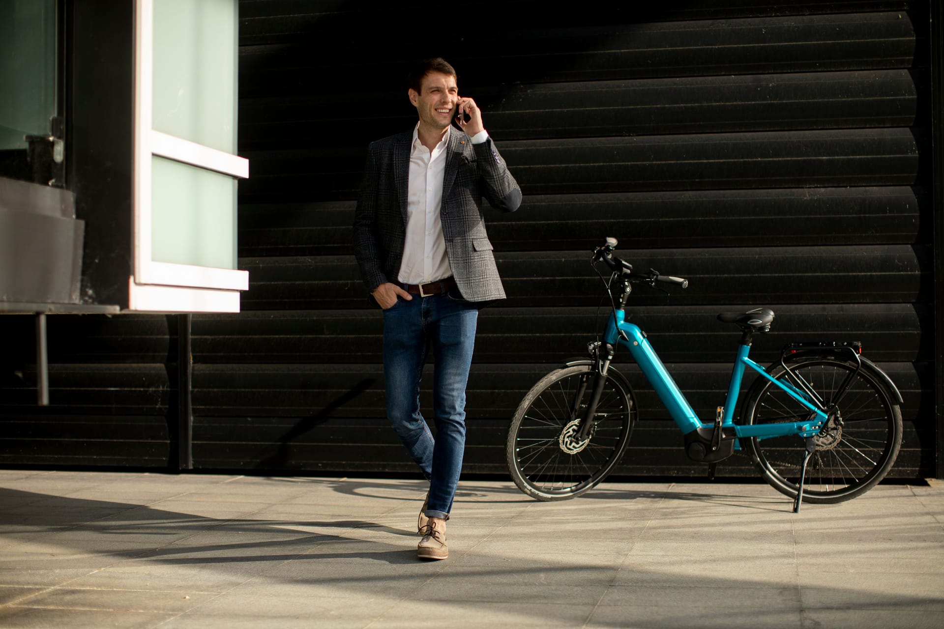 Young businessman walking away from the ebike and using mobile phone