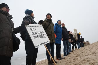 Einheimische und Feriengäste Hand in Hand am Strand auf Sylt: Auf dem Plakat steht "Sylt. Oben links. Nicht rechts!"
