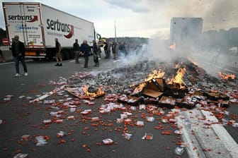 Frankreich: Protestierende Menschen stehen neben brennenden Tomaten-Paletten auf der Straße.