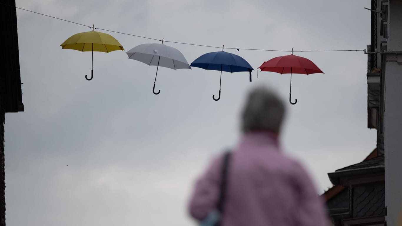 Regenschirme hängen als Dekoration in der Innenstadt vor einem grauen Himmel.