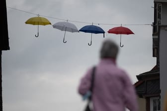 Regenschirme hängen als Dekoration in der Innenstadt vor einem grauen Himmel.
