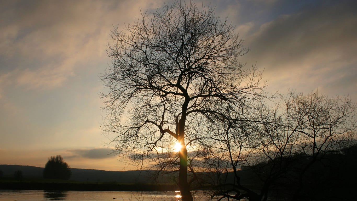 Sonnenuntergang über einem See (Symbolbild): Neben bewölktem Wetter kommt es zum Wochenbeginn auch periodisch zu sonnigen Abschnitten.