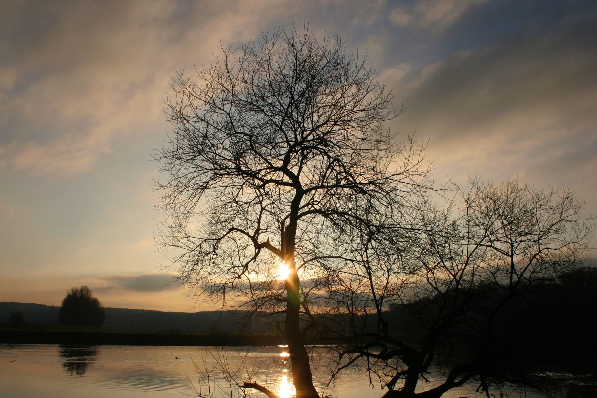 Sonnenuntergang über einem See (Symbolbild): Neben bewölktem Wetter kommt es zum Wochenbeginn auch periodisch zu sonnigen Abschnitten.