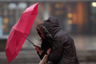 Passantin kämpft während eines starken Regenschauers mit Sturmböen mit ihrem Regenschirm (Symbolbild): Ein Sturmtief und ein Island-Tief sorgen für Regen und stürmischen Wind in Deutschland.