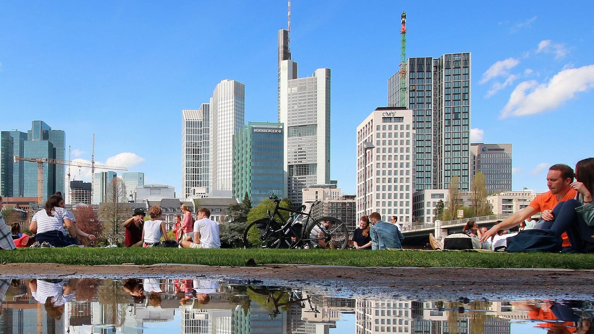 Frühlingswetter in Frankfurt (Symbolbild): Sonnenhungrige genießen die Sonnenstrahlen am Mainufer vor der Skyline.