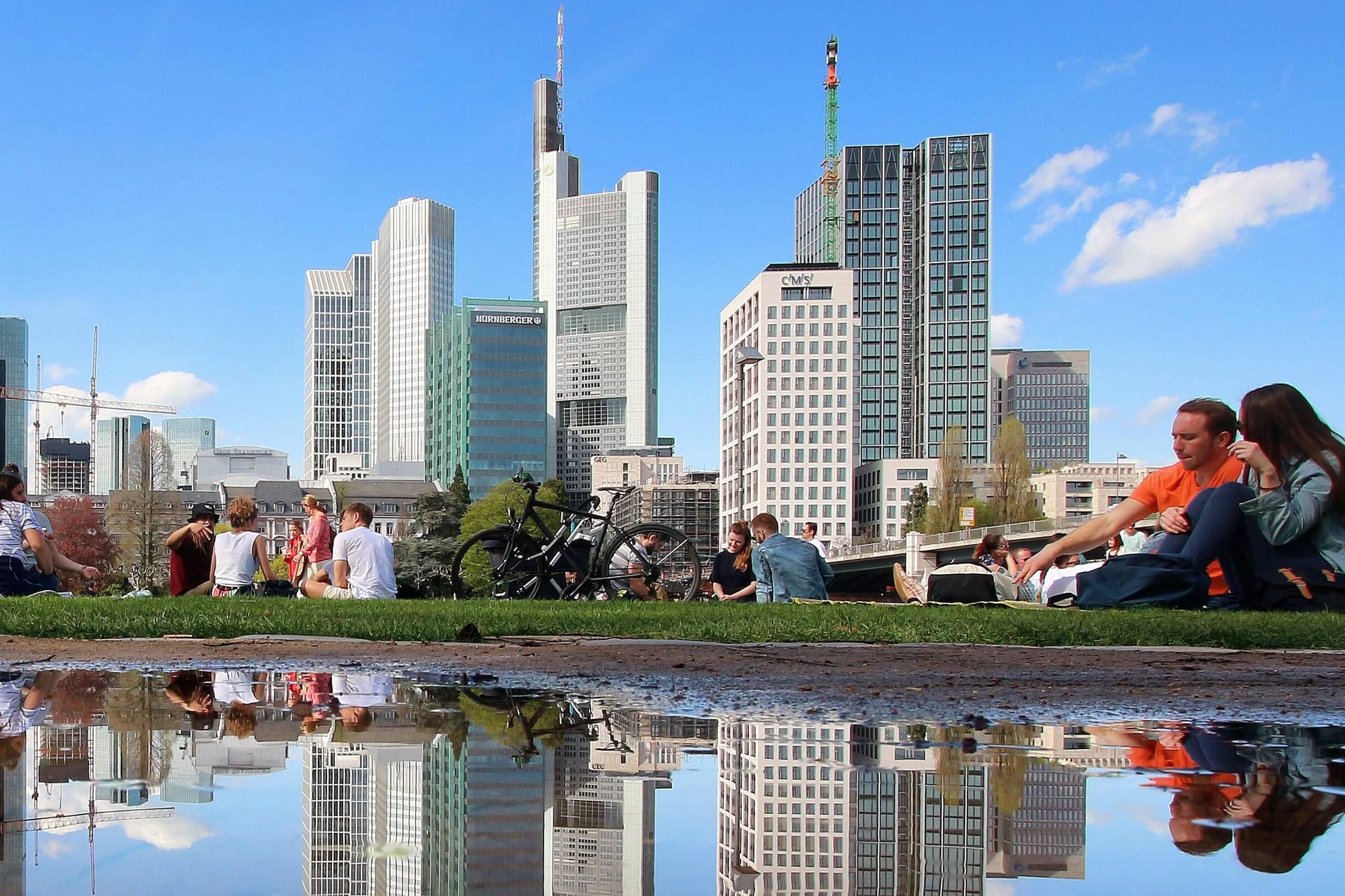 Frühlingswetter in Frankfurt (Symbolbild): Sonnenhungrige genießen die Sonnenstrahlen am Mainufer vor der Skyline.