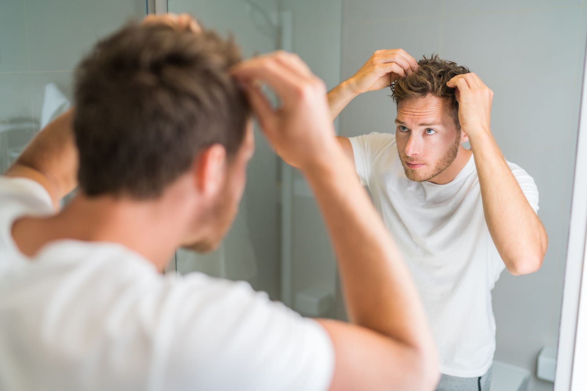 Ein Mann steht vor dem Spiegel und richtet seine Haare