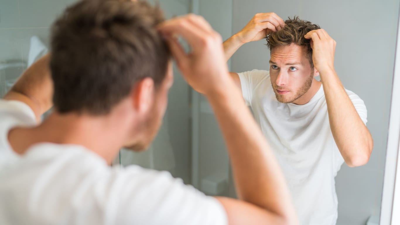 Ein Mann steht vor dem Spiegel und richtet seine Haare