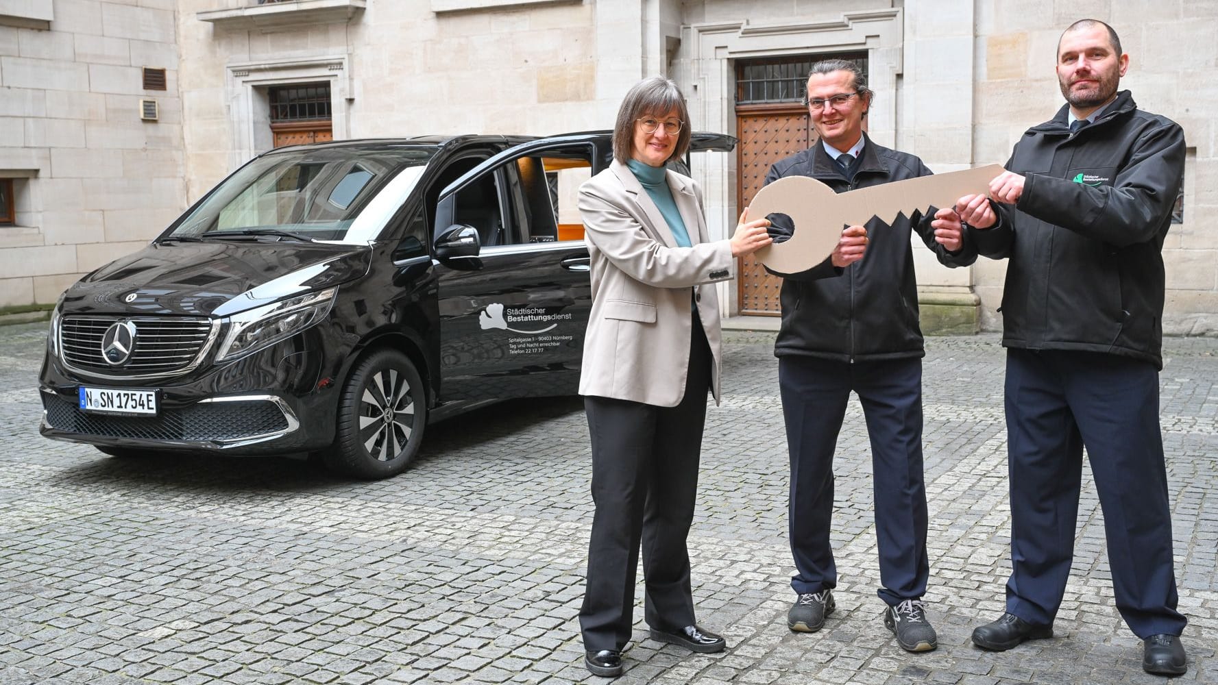 Umweltreferentin Britta Walthelm übergibt im Rathausinnenhof den ersten vollelektrischen Leichenwagen an die beiden zukünftigen Fahrer des Bestattungsinstituts der Stadt Nürnberg.