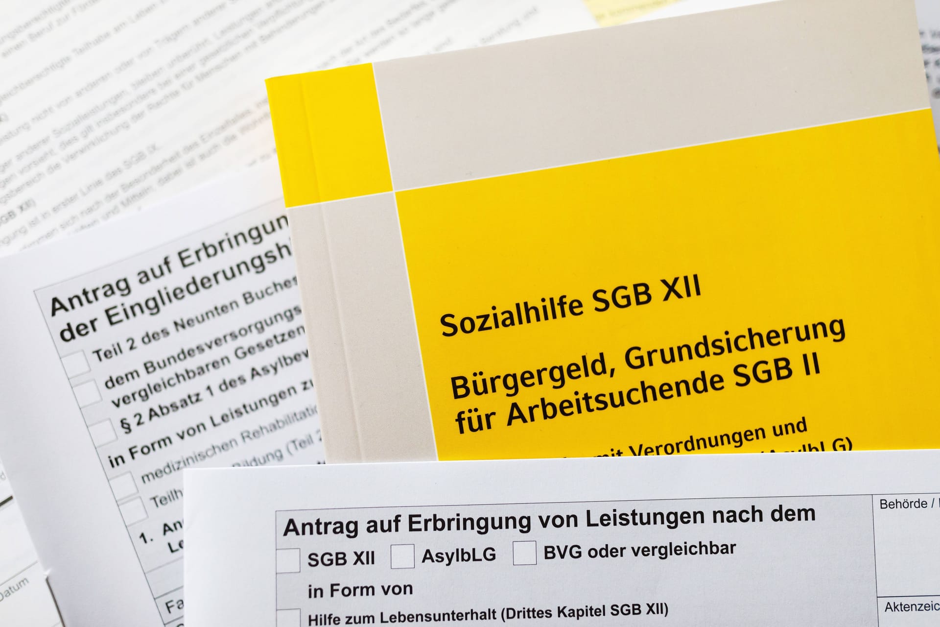 Ein Sozialgesetzbuch und verschiedene Antragsformulare (Symbolbild): Die Angeklagten hatten jahrelang Hartz IV in Bremen bezogen, obwohl sie nicht in Deutschland lebten.