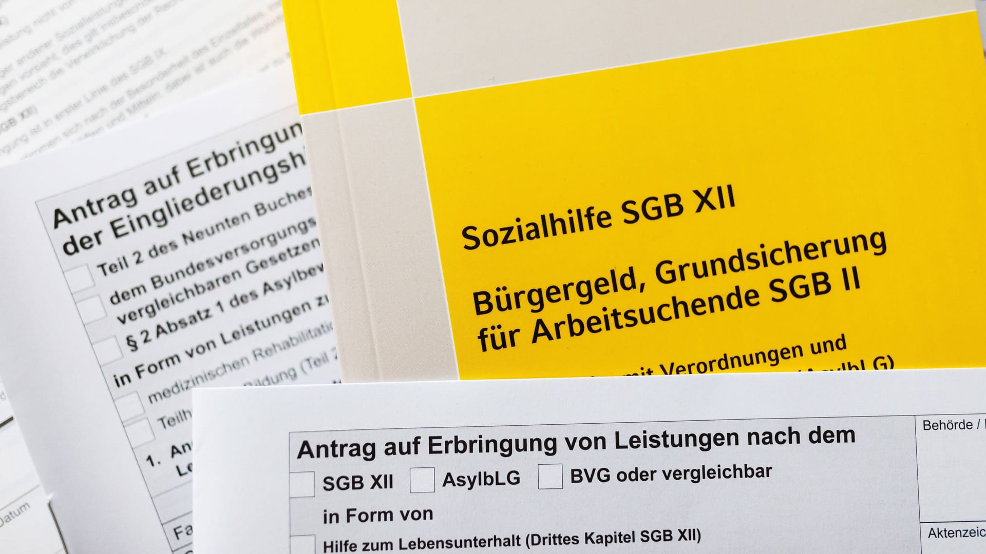 Ein Sozialgesetzbuch und verschiedene Antragsformulare (Symbolbild): Die Angeklagten hatten jahrelang Hartz IV in Bremen bezogen, obwohl sie nicht in Deutschland lebten.