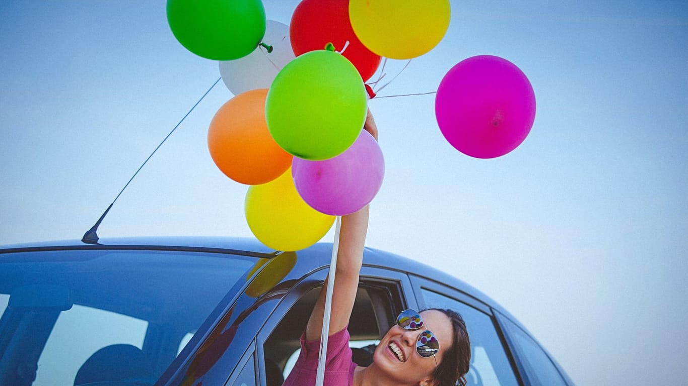 Eine Frau hält einen Ballonstrauß, während Sie sich aus dem Fenster ihres Autos lehnt