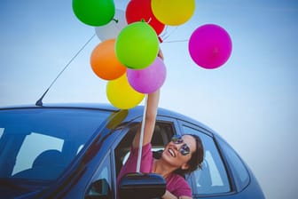 Eine Frau hält einen Ballonstrauß, während Sie sich aus dem Fenster ihres Autos lehnt