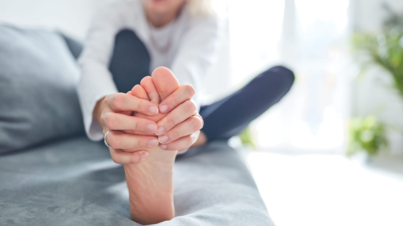 Eine Frau umfasst den schmerzenden Fuß mit den Händen: Beim Sjögren-Syndrom können sich verschiedene neurologische Symptome einstellen, zum Beispiel Schmerzen oder Missempfindungen in den Füßen.