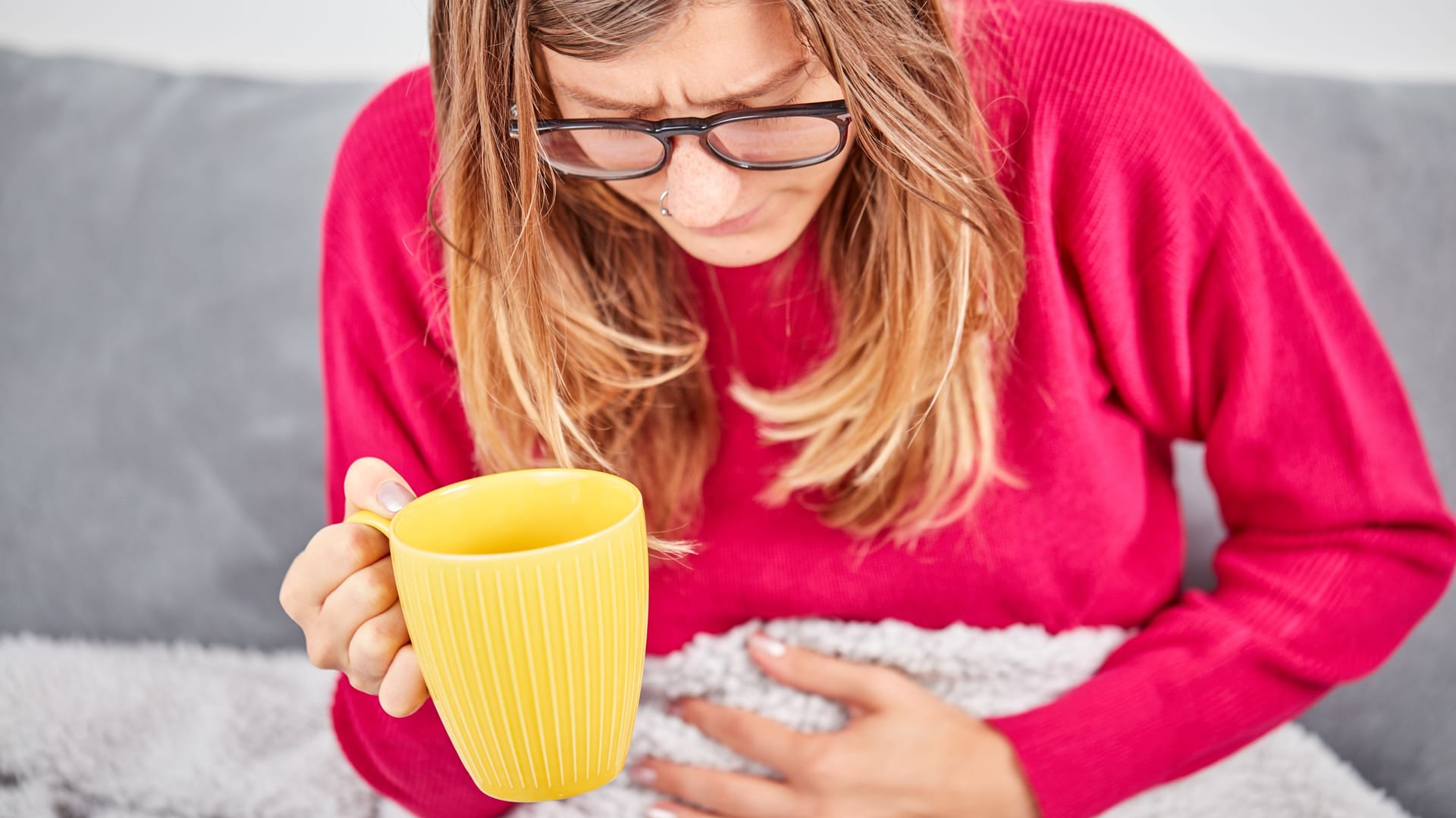 Frau hält eine Tasse in der Hand und hat Bauchschmerzen