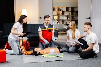 Young man instructor helping to make first aid heart compressions with dummy during the group training indoors