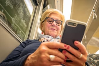 Eine Frau mit ihrem Smartphone in der Hand (Archivbild): Das Handynetz in der Berliner U-Bahn soll endlich für alle besser werden.