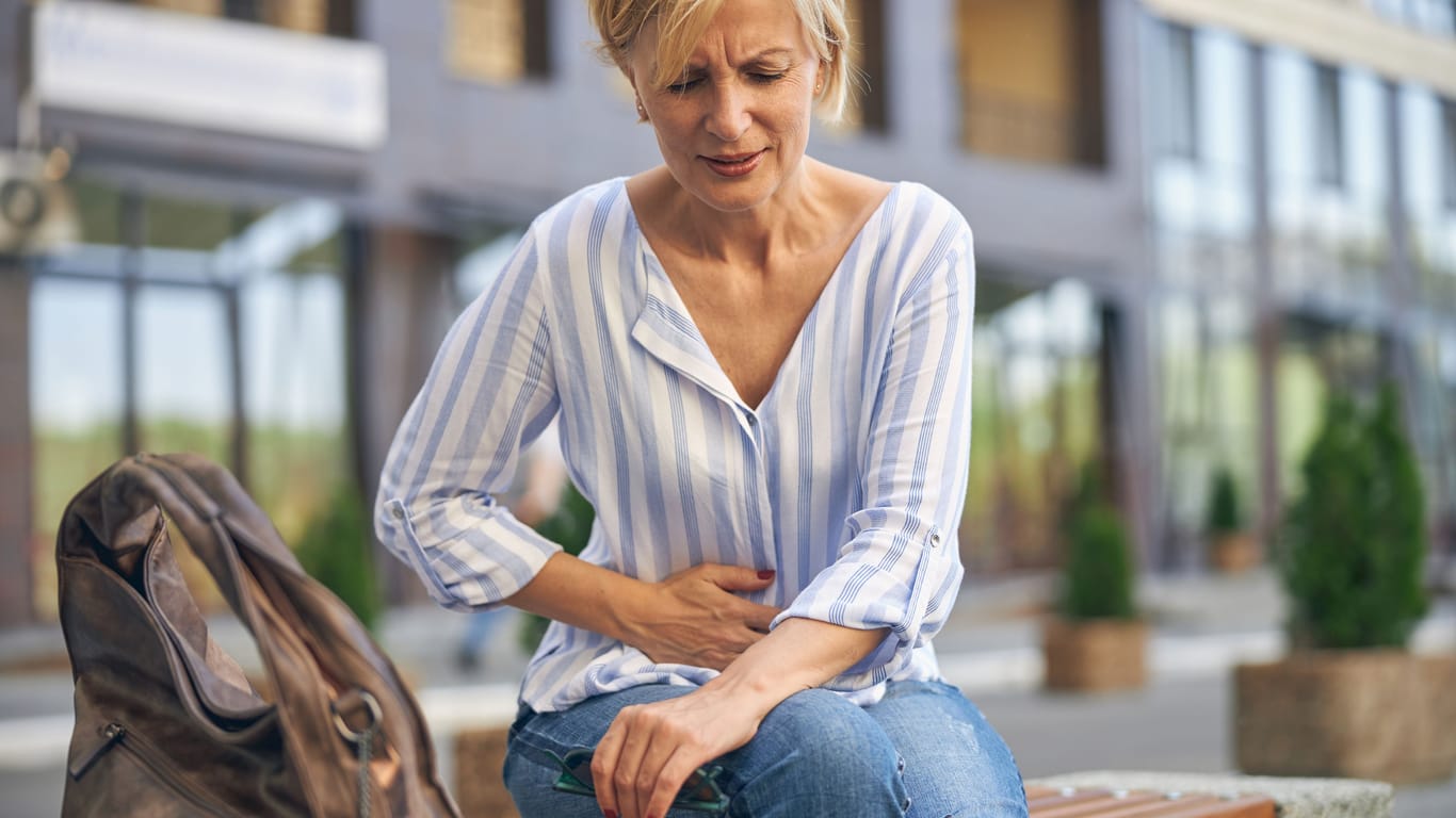 Eine Frau fasst sich an den Bauch: Zeigen sich beim Sjögren-Syndrom Darmprobleme, kann ein Zusammenhang mit der Autoimmunerkrankung bestehen.