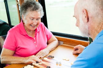 Zwei ältere Menschen spielen Backgammon zusammen an einem Tisch.