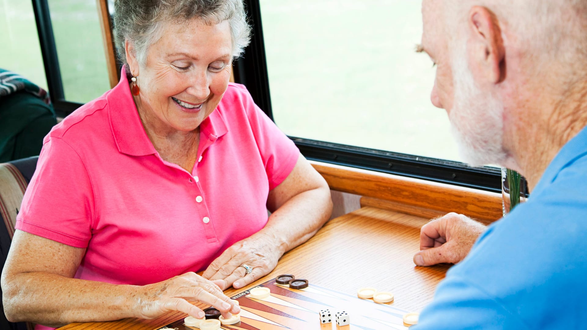 Zwei ältere Menschen spielen Backgammon zusammen an einem Tisch.