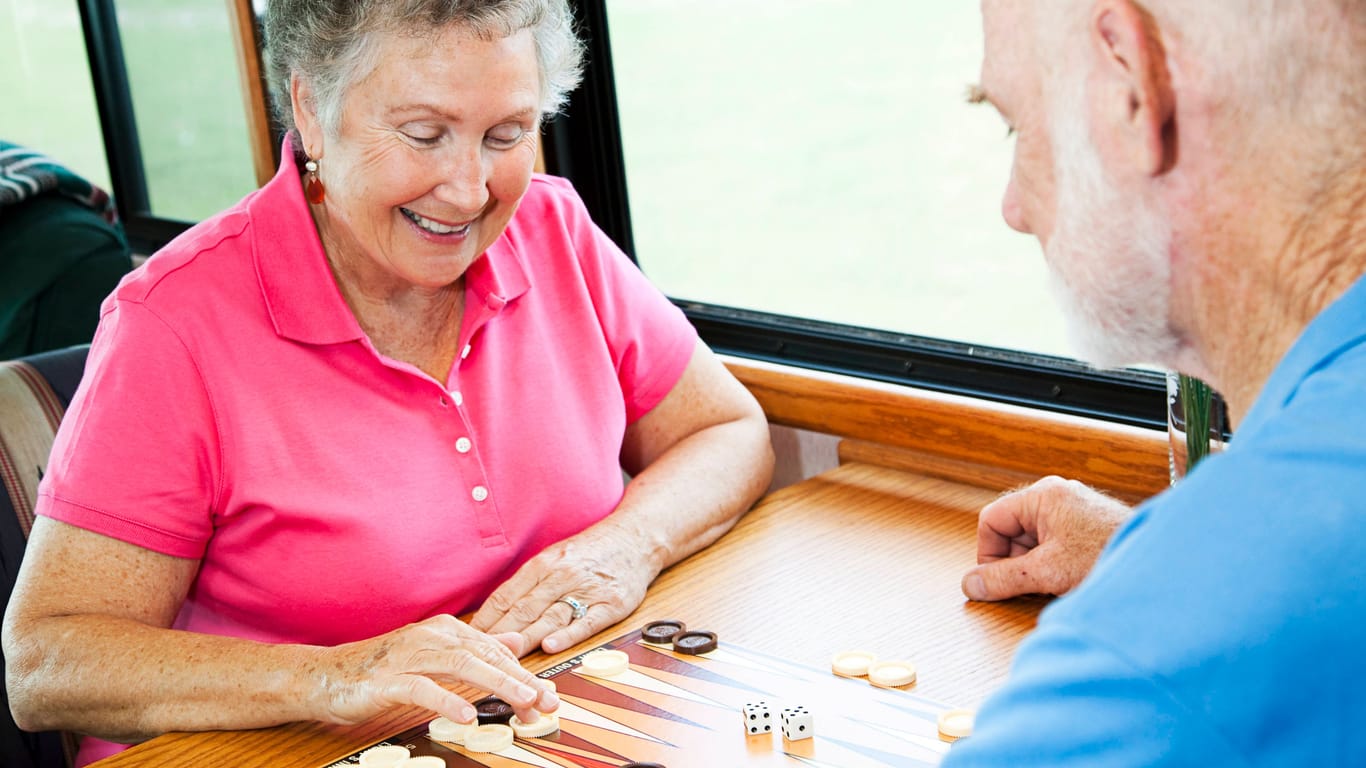 Zwei ältere Menschen spielen Backgammon zusammen an einem Tisch.
