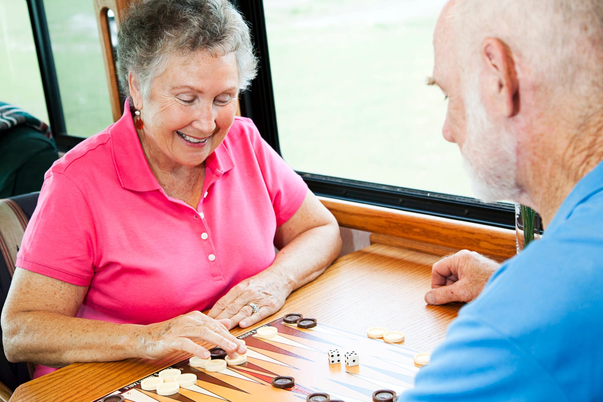 Zwei ältere Menschen spielen Backgammon zusammen an einem Tisch.